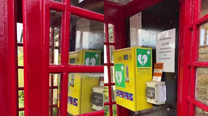 在英国，一个男人的手打开了一个红色电话亭的门，这个电话亭被改造成了一个除颤器亭。垂直4k慢动作。社区