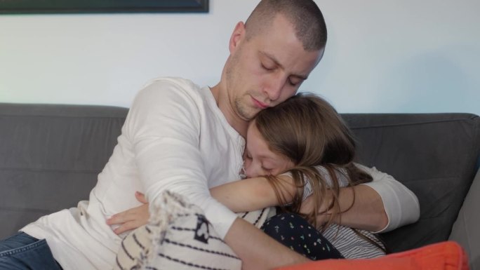 一位父亲抱着他伤心的、撅着嘴的小女儿，安慰着她