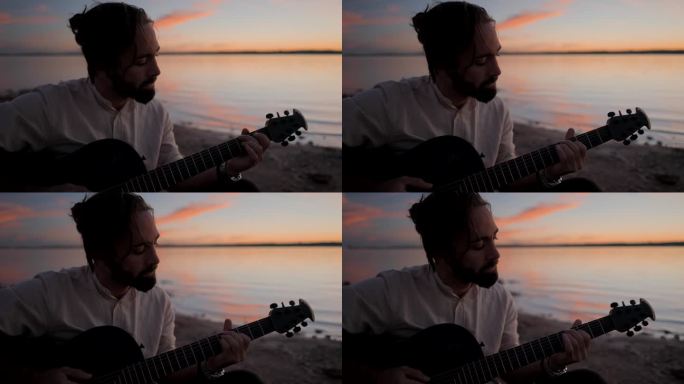 深思熟虑的蓄着胡子的潮人在湖边对着夕阳的天空弹着原声吉他——慢镜头肖像