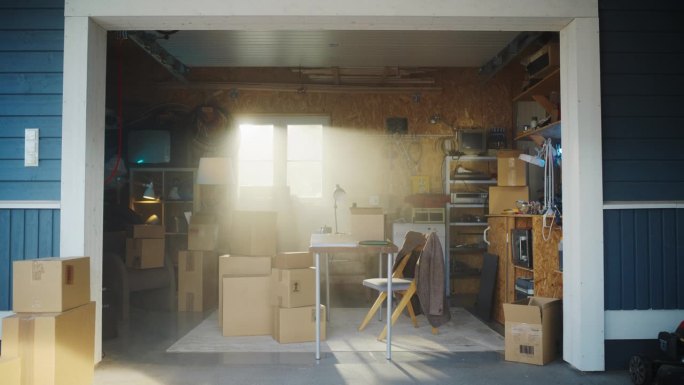 在复古车库中建立小企业主空办公桌的镜头。纸板箱与产品包装运输给客户躺在周围。家族企业与创业概念。