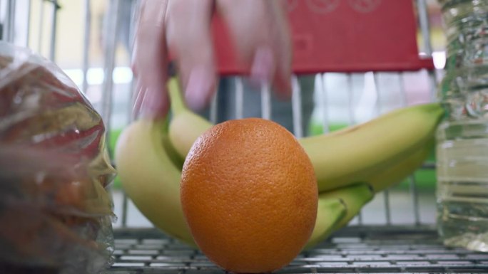 超市里一个推着手推车的女人把一个橙子和香蕉放进去。