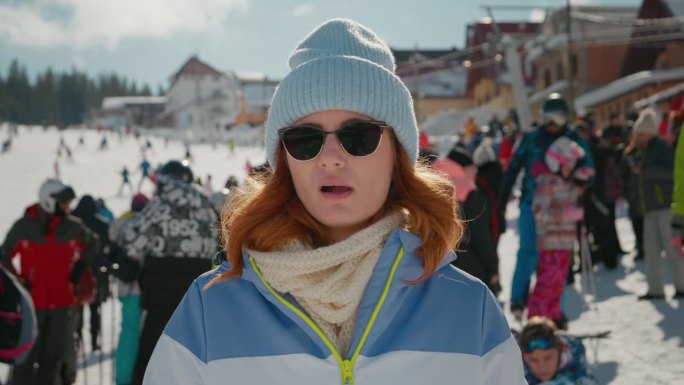 一个粗心的女人站在山上的滑雪道上嚼口香糖。