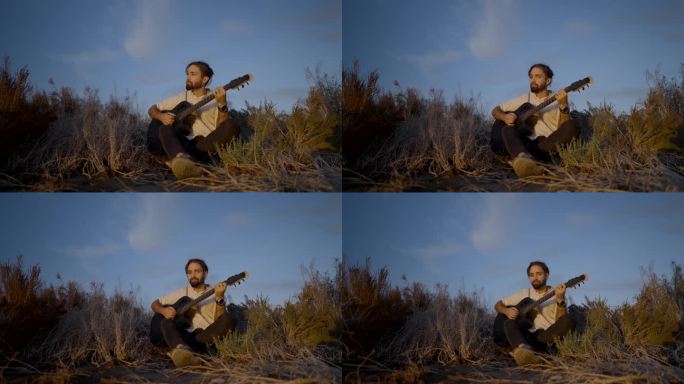 一个年轻人坐在草地上，在日落时分弹着吉他——慢镜头回放