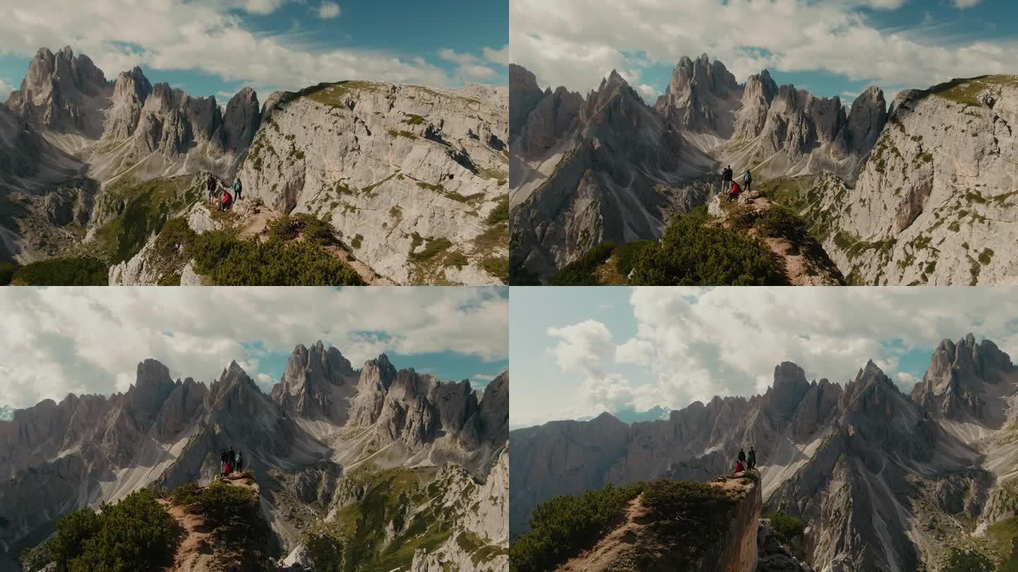 视差无人机拍摄与游客观看全景与高大陡峭的岩石山脉，部分云的天空为背景，在阿尔卑斯山徒步旅行，雄伟的景