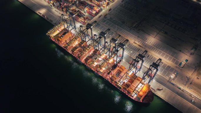 集装箱货船夜间在工作吊桥上装卸货物，用于商业物流进出口运输或货物运输。
