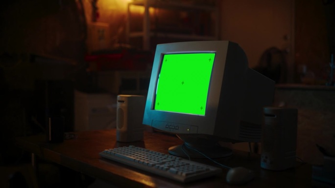 互联网爱好者空荡荡的工作场所:深夜，站在复古车库的桌子上，展示着绿屏Chromakey的旧台式电脑。