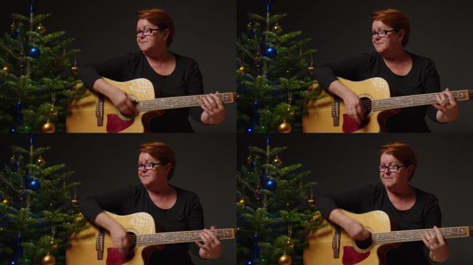 一名女子坐在地板上，用吉他弹着圣诞歌曲，旁边是装饰着花环灯的新年树