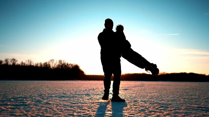 无价的为人父母时刻。夕阳下，快乐的爸爸和小儿子在冬日公园里奔跑。冬天公园里美丽的日落。
