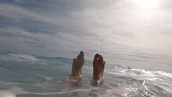 年轻女子在海浪中游泳，可以看到她的脚