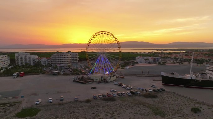 夏日日落时的Les Barcares海滩鸟瞰图。旅游旺季，海滩上有一座摩天轮和一艘巨轮作为吸引游客的