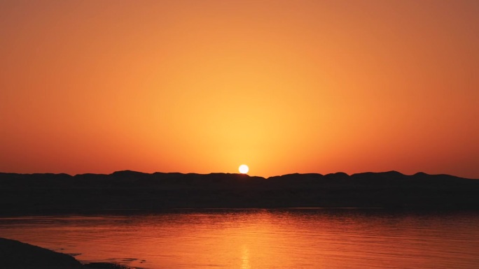 海岸上红色黎明的奇妙时间间隔。太阳从海滩上的山上升起