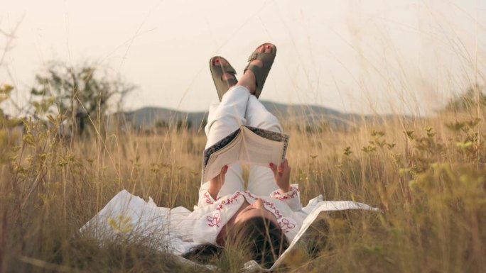日落时分，一个女人在草地上翘着脚看书