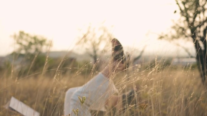 日落时分，一名身穿白衣的女子在草地上抬起脚