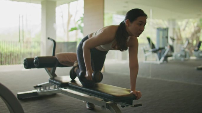 亚洲妇女在健身房锻炼时使用哑铃