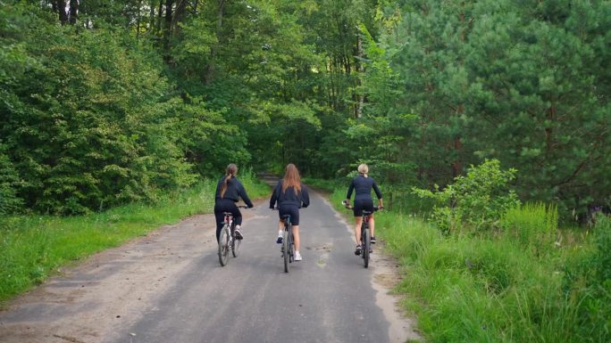 享受夏日周末，三个女人在大自然中骑自行车，在阳光明媚的日子里骑在森林里