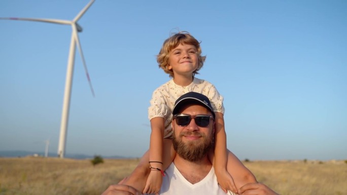 一个男人背着他的小女孩走在风电场里。快乐父女共度美好时光，共享清新空气，共创更环保、可持续、高效的能
