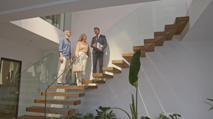一位男性房地产经纪人和他的客户在豪宅里走上楼梯