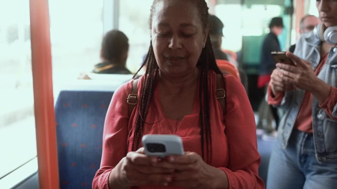 年长的非洲妇女坐在电车里玩手机