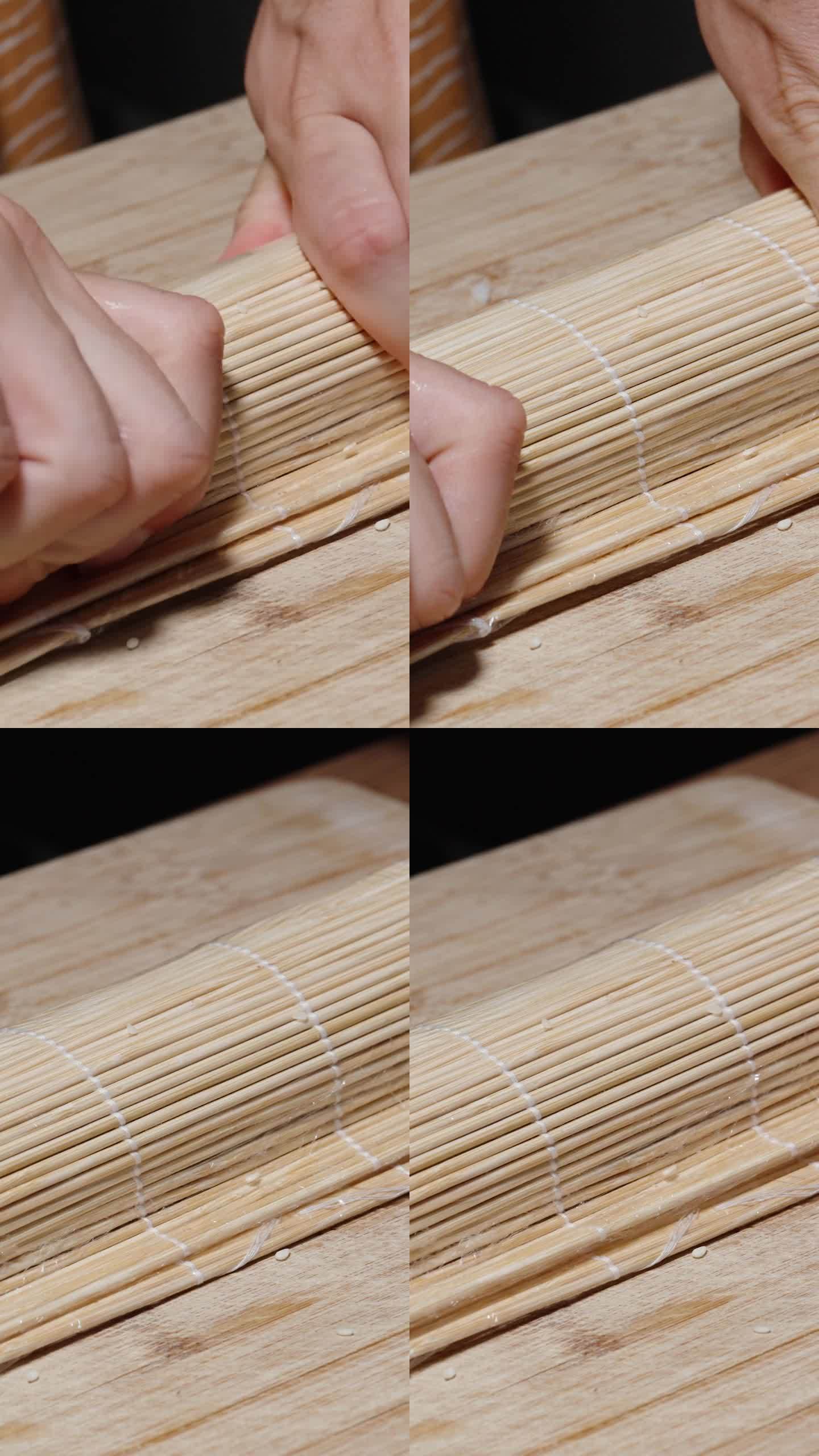 垂直视频。这个女人用竹席把寿司卷起来，然后用力按压。