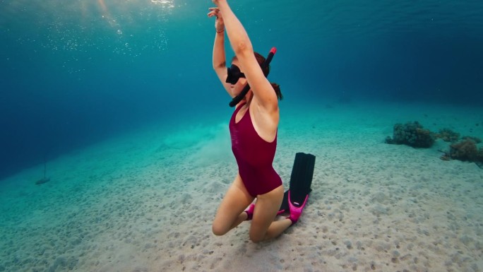 一名身穿粉色潜水服的女子在水下摆姿势，然后浮出水面