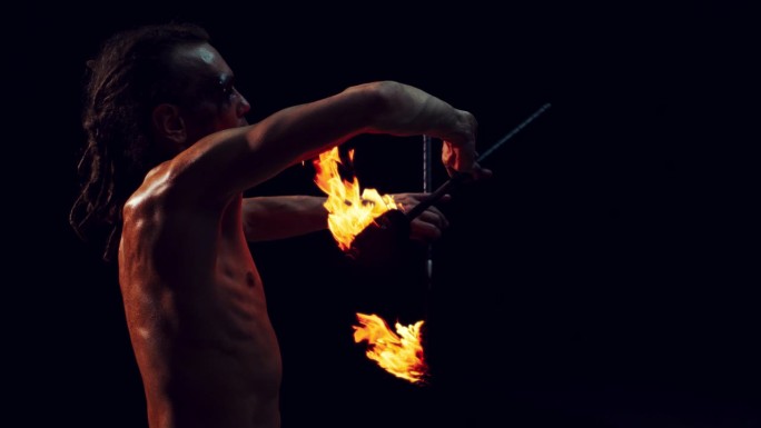 一个在黑暗的工作室里玩弄两个火把的火焰艺术家的肖像。在灯光节或嘉年华的舞台上，一个火焰表演者表演的超