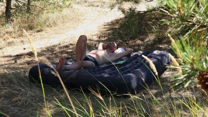 在阳光明媚的森林里，一名男子在充气床垫上睡觉