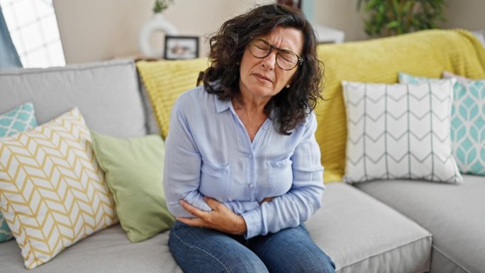 中年西班牙妇女胃痛坐在家里的沙发上