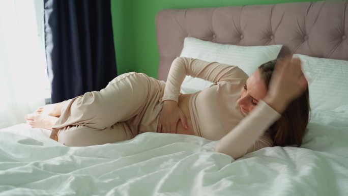 女性疼痛或月经综合症。一名年轻女子躺在家里的床上，捂着肚子克服痉挛。