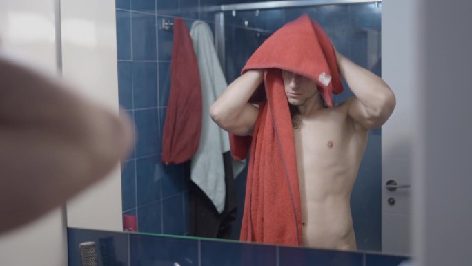 年轻的都市美男淋浴后用红毛巾在浴室镜子前擦干头发-中景