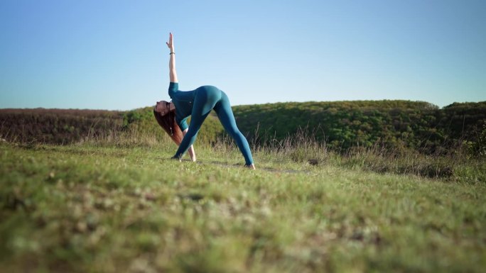 一位女瑜伽士在高山之巅做瑜伽练习——在深呼吸的情况下做三角体式。野性的自然，自由的人类。自由，健康的