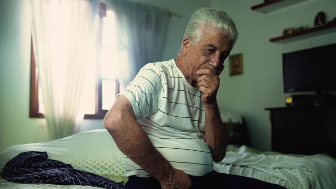 一位忧心忡忡的老人坐在床边沉思，与内省的思想和沉思的表情作斗争