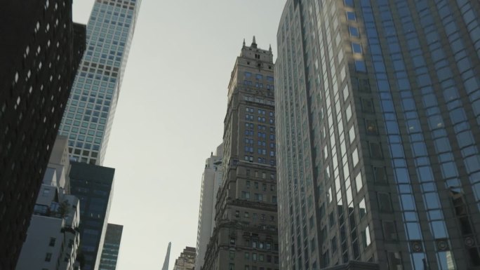 商业摩天大楼的低角度镜头从另一座办公大楼的窗户反射。在一个晴朗的晴天，从一辆移动的汽车上拍摄的纽约城