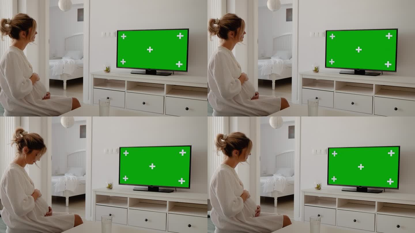 孕妇坐在家里的茶几上注视着绿屏电视。