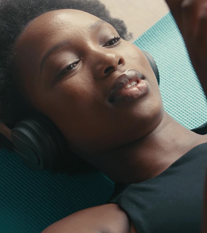 放轻松，在健身房地板上给戴着耳机的黑人女人打电话，听音乐、发短信或玩社交媒体。智能手机、应用程序和非