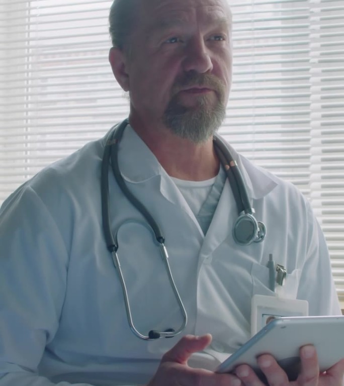 带着数码平板电脑的成熟医生在病房里与病人交谈