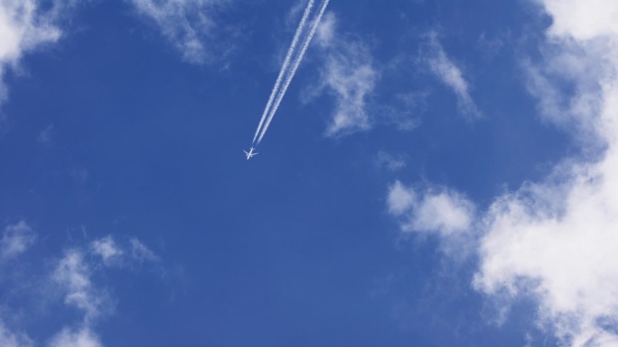 带着凝结尾迹的飞机在蓝天上飞行