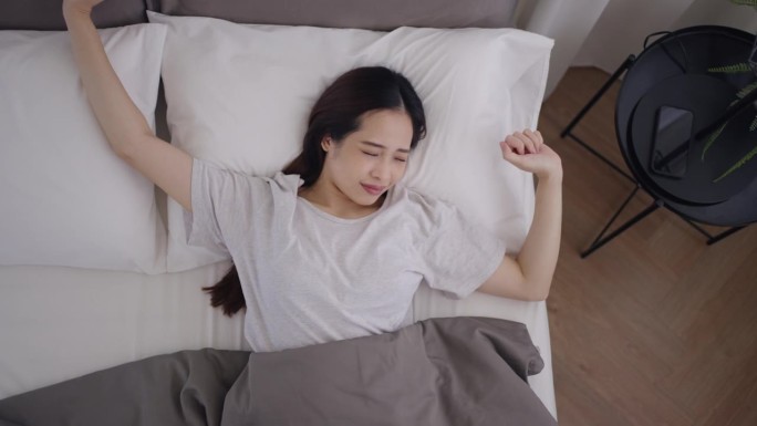 一个亚洲女人醒了周末自然醒伸懒腰白色床单