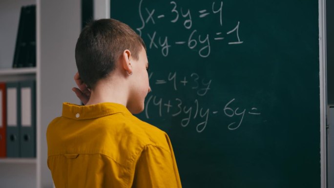 一个十几岁的男孩试图在黑板旁解数学方程，抓耳挠腮