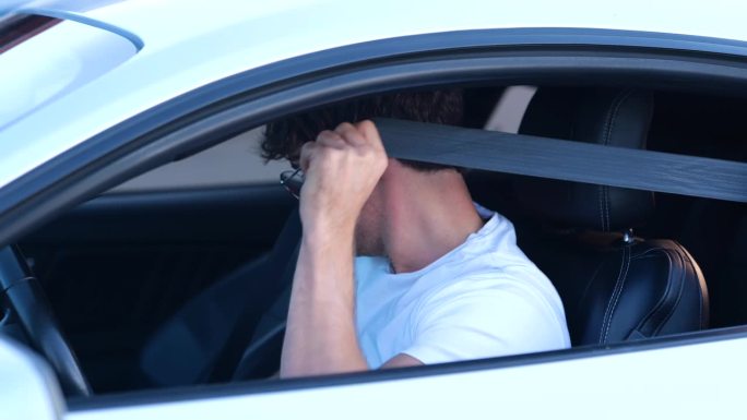 戴眼镜的年轻白人男子系好安全带，坐在打开车窗的汽车上。慢动作