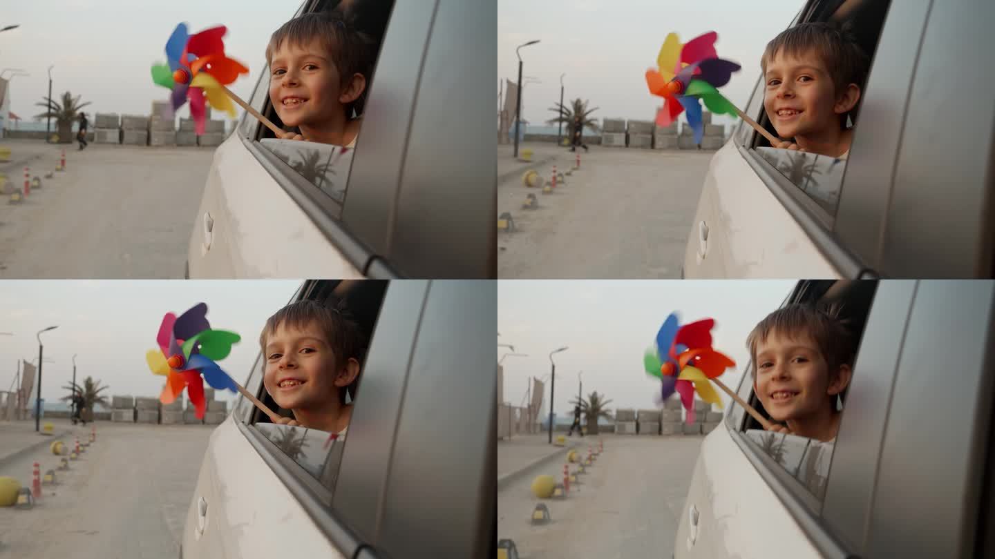 可爱活泼的小男孩拿着彩色的风车，透过打开的车窗看日落
