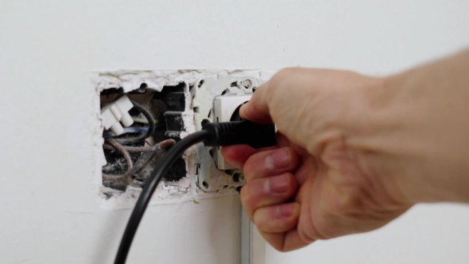 危险地从一个危险的破损的插座上拔下电源插头，靠近墙上的电线被撕破