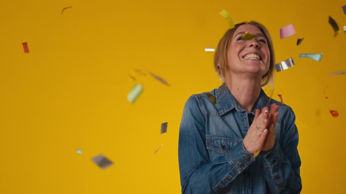 工作室拍摄的兴奋的女人庆祝大胜在黄色背景上的金属丝五彩纸屑淋浴