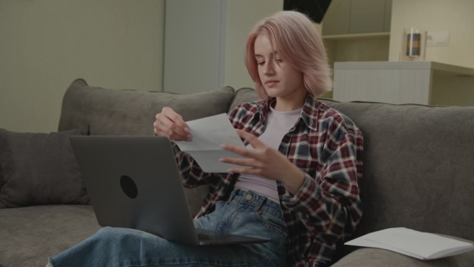 看着笔记本电脑处理文件的女性。20多岁的企业家在家办公室管理文件、发票、税单。