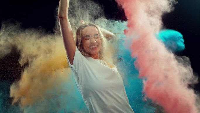 一个美丽快乐的女孩笑着庆祝胡里节的动作肖像。穿着白衬衫的年轻女性被彩色的黄、粉、蓝粉末漆覆盖。工作室