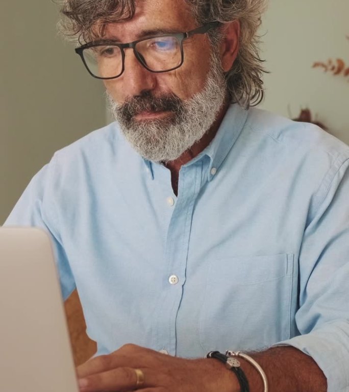 头发花白的中年男子坐在客厅里使用笔记本电脑