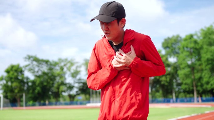 亚洲跑步者在跑道上跑步后心脏病发作或胸痛。疲惫的运动员受到心脏紧张的折磨。保健和运动的理念。