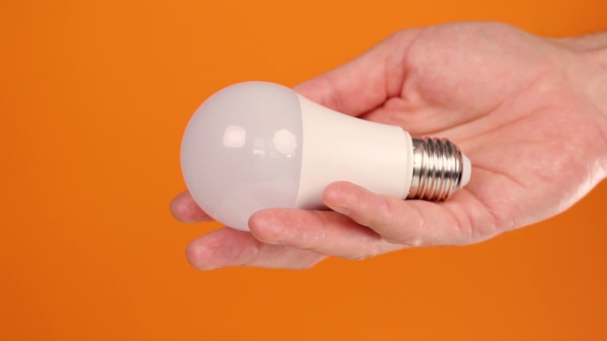 创意明亮的电力节能灯泡在节省者的手在极简的颜色橙色背景近距离