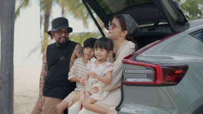 一个亚洲家庭坐在敞篷汽车的后座上，一起在海滩上度假的快乐时光。