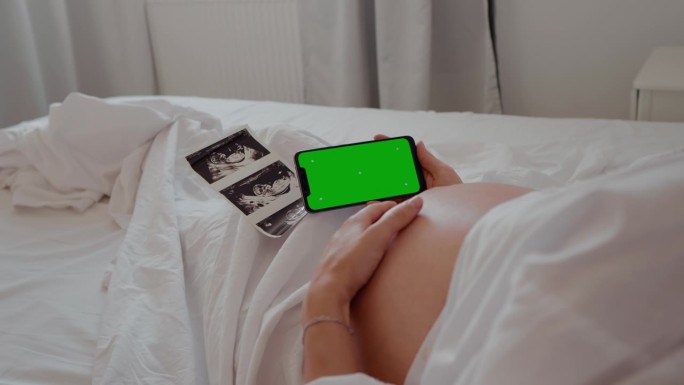 孕妇手持绿色色度键屏的手机触摸腹部。