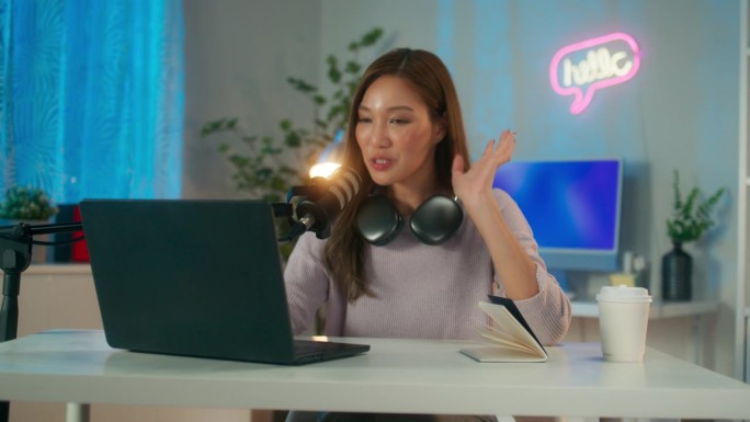 快乐的年轻亚洲女性电台主持人或播客，戴着耳机在麦克风上说话，在家庭工作室里运行播客